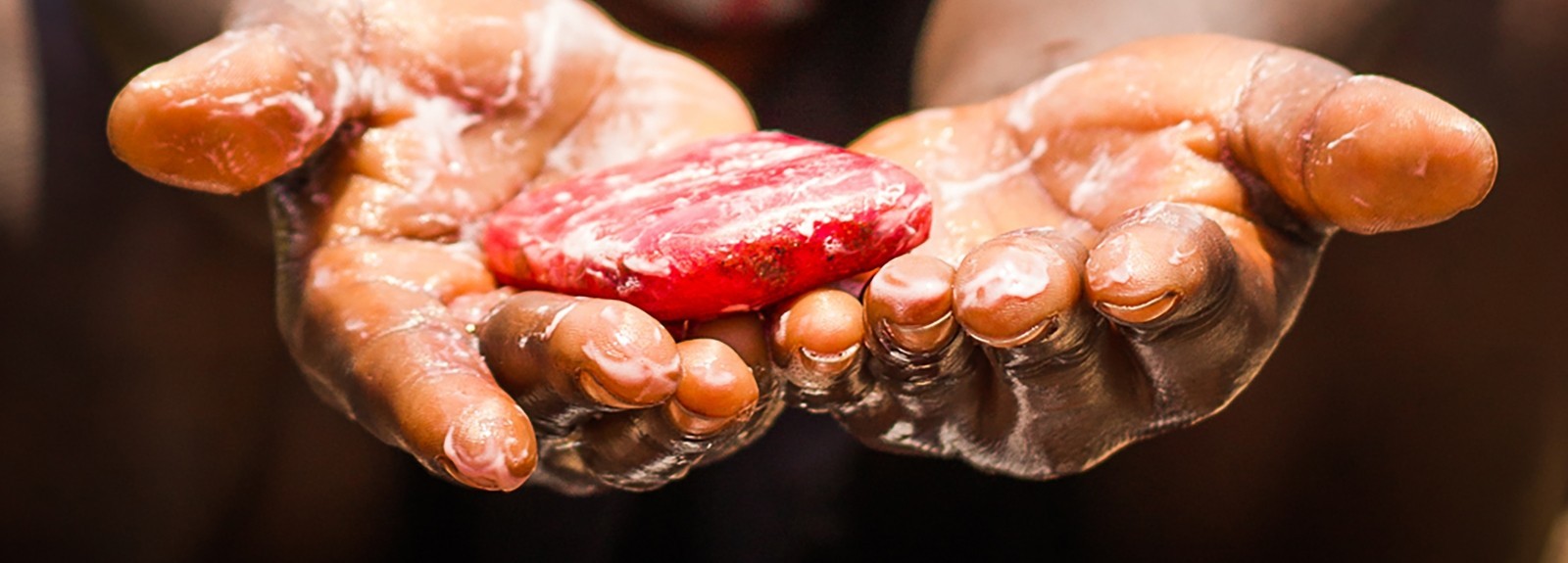 A child's soapy hands are outstretched holding a red bar of soap