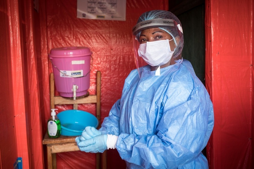 A nurse dressed in full blue protective equipment scrubs up in front of a water jug/basin