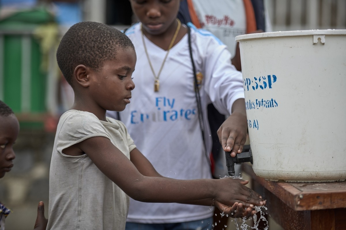 A young Congolese boy washes his hands using water coming out of a white bucket