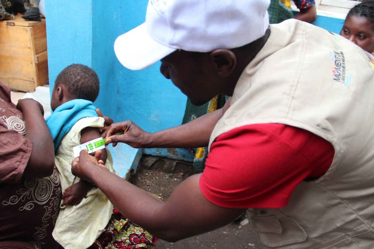 Community health worker Thierry Kasereka screens a child for malnutrition through IMA World Health's MOMENTUM Integrated Health Resilience.