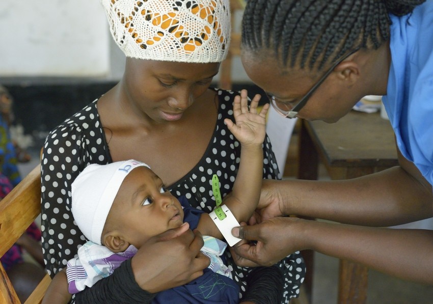 A nurse measure the arm circumference of a baby in his mother's arms.