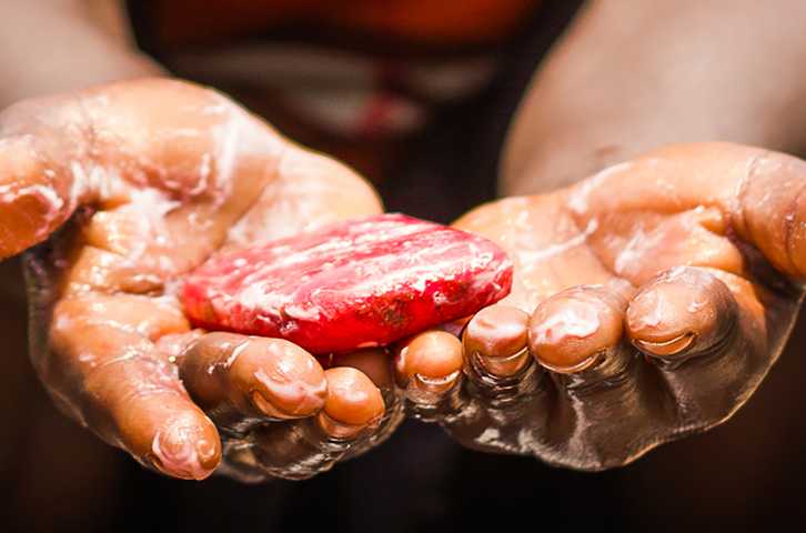 A child's soapy hands are outstretched holding a red bar of soap