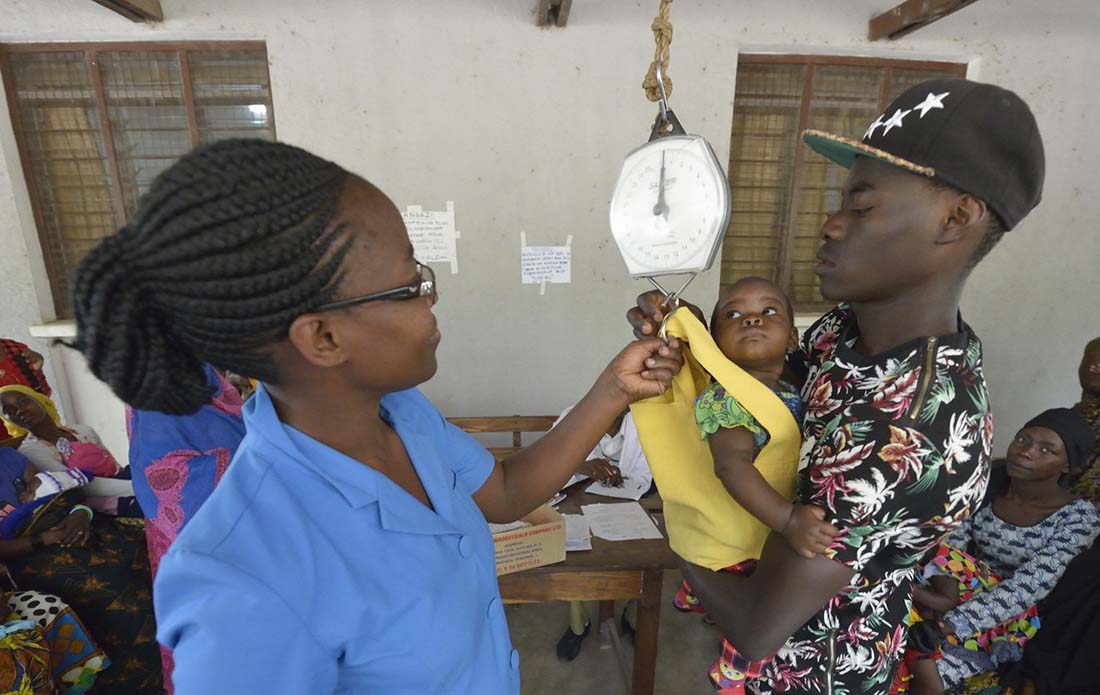 Nurse Praxeda Kahwa helps Jumanne Kessy hoist his daughter Esther onto a scale in the Nyamagana District Hospital in Mwanza Tanzania. The child and others were weighed as part of a nutrition screening program at the hospital. (Photo by Paul Jeffrey/IMA World Health)